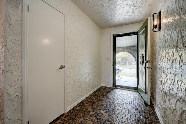 foyer entrance featuring a textured wall, baseboards, brick patterned floor, and a textured ceiling