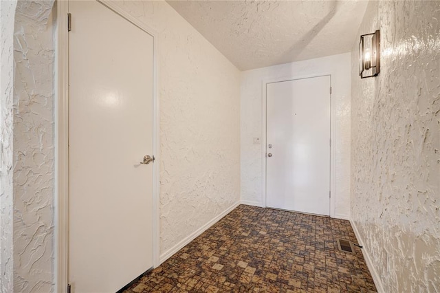 interior space featuring visible vents, baseboards, a textured ceiling, and a textured wall