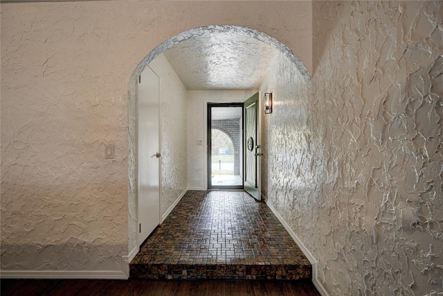 foyer entrance featuring wood finished floors, baseboards, arched walkways, a textured ceiling, and a textured wall