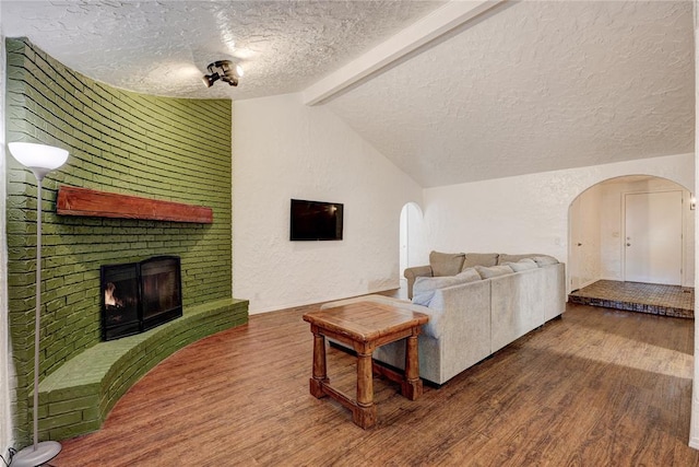 living room with arched walkways, a brick fireplace, wood finished floors, and vaulted ceiling with beams