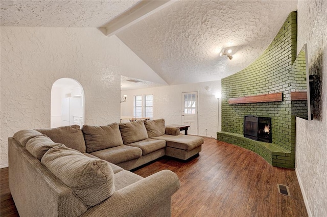 living area featuring a brick fireplace, vaulted ceiling with beams, a textured wall, wood finished floors, and a textured ceiling