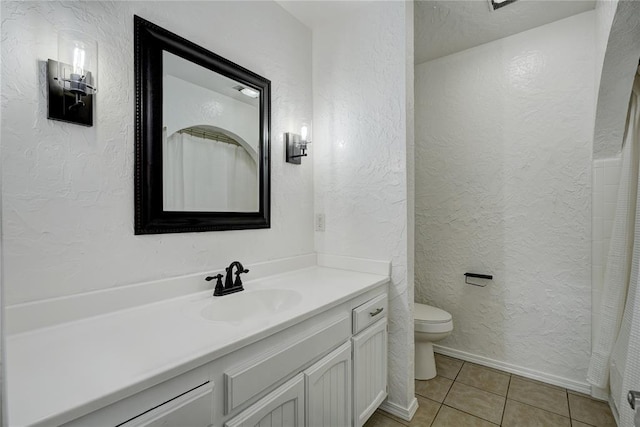 bathroom featuring tile patterned floors, toilet, vanity, and a textured wall