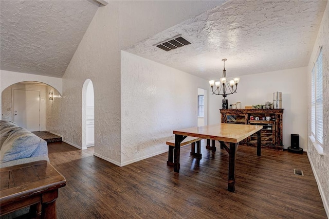 dining space featuring a textured wall, visible vents, an inviting chandelier, and wood finished floors