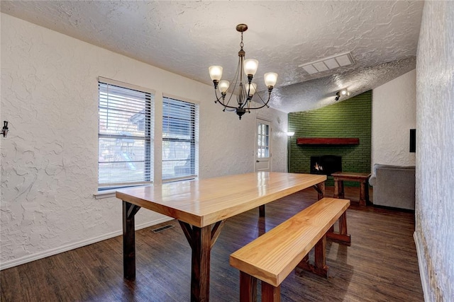 dining room with wood finished floors, a brick fireplace, a notable chandelier, and a textured wall