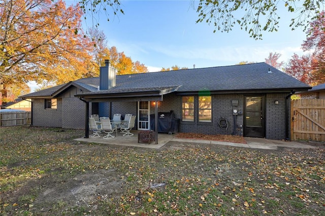 rear view of property featuring a patio area, a chimney, brick siding, and fence