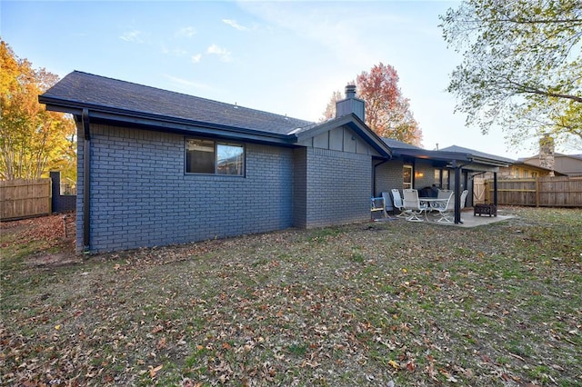 back of property featuring fence, brick siding, a chimney, a patio area, and a lawn