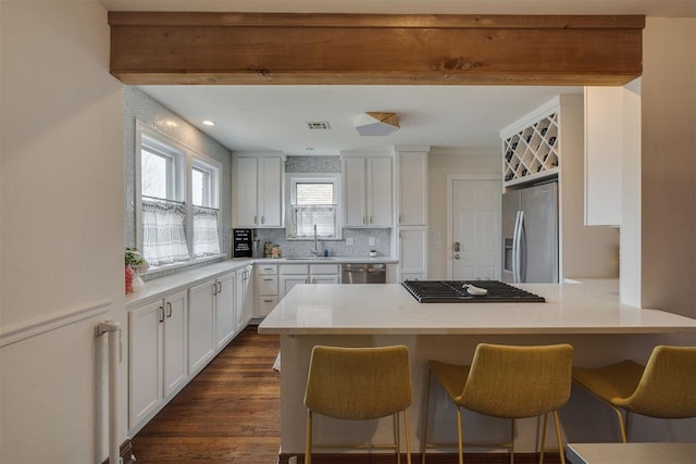 kitchen with visible vents, white cabinetry, stainless steel appliances, a peninsula, and a breakfast bar area