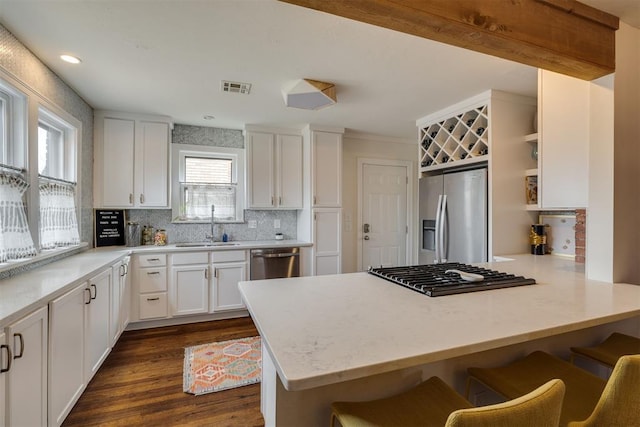 kitchen with a peninsula, a sink, white cabinets, appliances with stainless steel finishes, and a kitchen breakfast bar