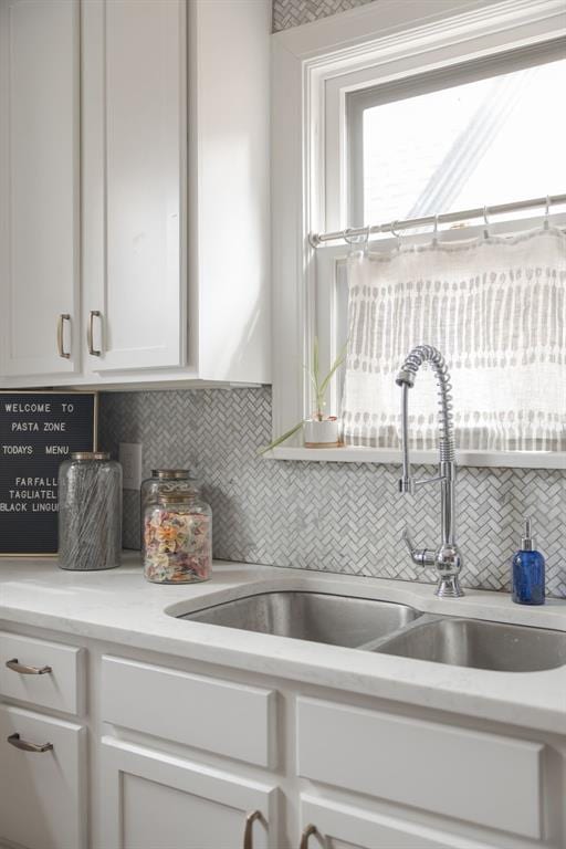 kitchen with light countertops, white cabinets, tasteful backsplash, and a sink