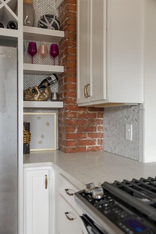 kitchen with open shelves, white cabinetry, gas range, decorative backsplash, and light stone countertops