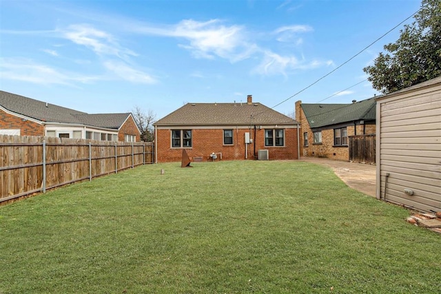 rear view of property with central AC unit, a fenced backyard, a chimney, a lawn, and brick siding