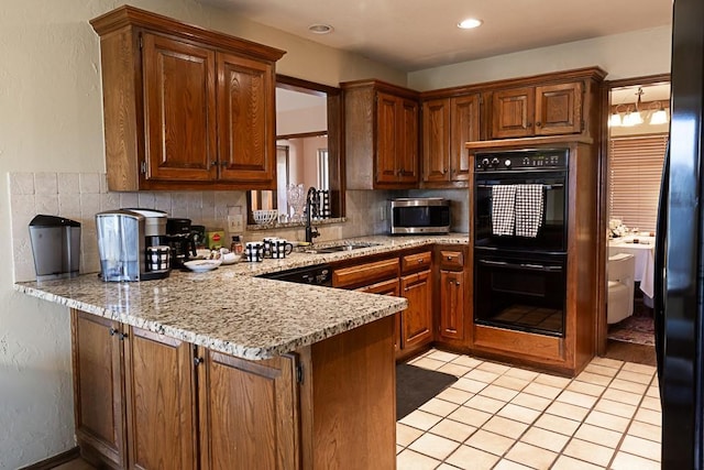 kitchen featuring brown cabinetry, a peninsula, dobule oven black, stainless steel microwave, and backsplash