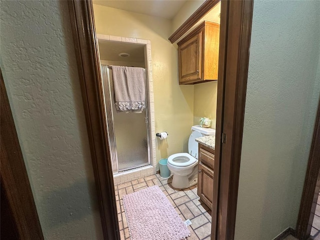 full bath with vanity, toilet, a shower stall, and a textured wall