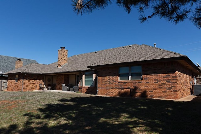 back of property featuring a lawn, brick siding, roof with shingles, and a chimney