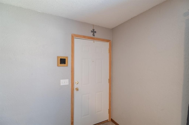 doorway featuring a textured ceiling and a textured wall