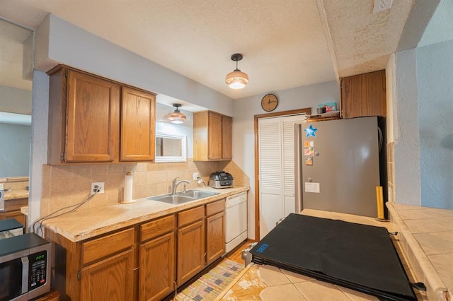 kitchen with a sink, backsplash, stainless steel appliances, brown cabinetry, and tile counters