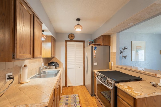 kitchen with tile countertops, appliances with stainless steel finishes, light wood-style floors, brown cabinetry, and a sink