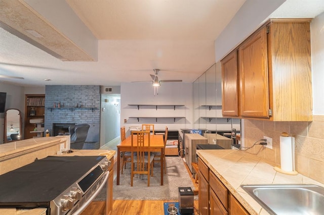 kitchen with visible vents, a ceiling fan, tile countertops, light wood finished floors, and a brick fireplace