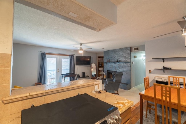 kitchen with visible vents, a fireplace, ceiling fan, tile counters, and french doors