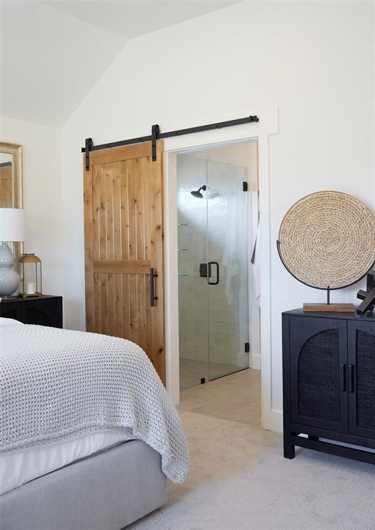 bedroom with light carpet, a barn door, and vaulted ceiling