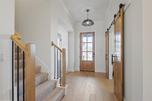 entryway with crown molding, baseboards, stairway, light wood-type flooring, and a barn door