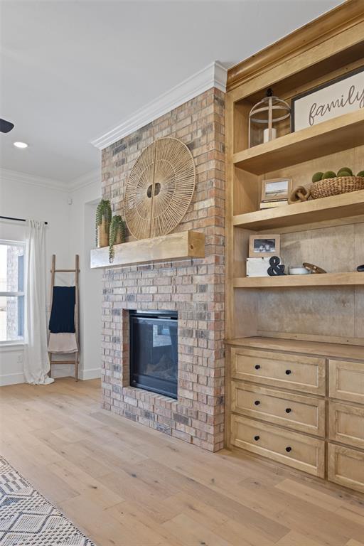 unfurnished living room featuring ornamental molding, built in features, light wood-style floors, baseboards, and a brick fireplace