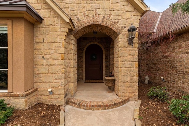 entrance to property featuring stone siding and a shingled roof