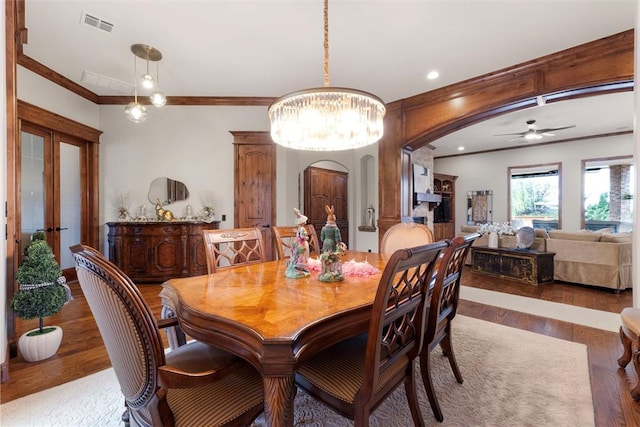 dining room featuring arched walkways, visible vents, ornamental molding, and wood finished floors