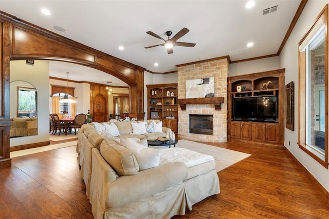 living area featuring visible vents, a stone fireplace, wood finished floors, and crown molding