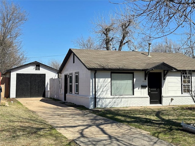 view of front facade featuring a shingled roof, brick siding, concrete driveway, and an outdoor structure