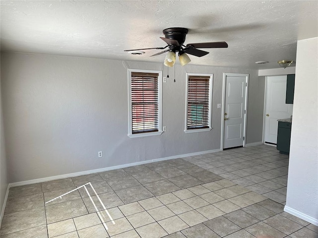 empty room featuring light tile patterned floors, a textured ceiling, baseboards, and a ceiling fan