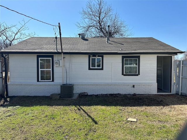 back of house with a lawn, a shingled roof, and central AC