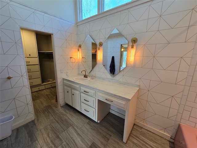 bathroom featuring a spacious closet, tile walls, vanity, and wood finished floors