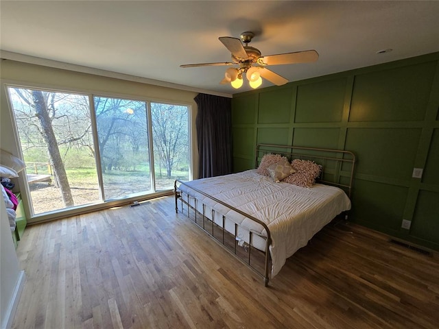 bedroom featuring access to outside, a decorative wall, wood finished floors, and ceiling fan