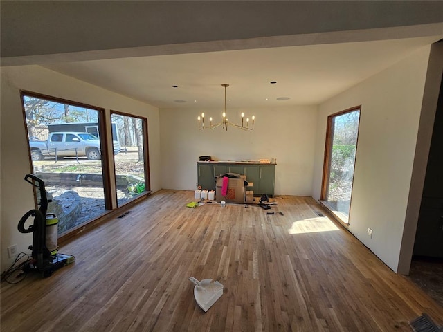 unfurnished dining area with visible vents, an inviting chandelier, and wood finished floors