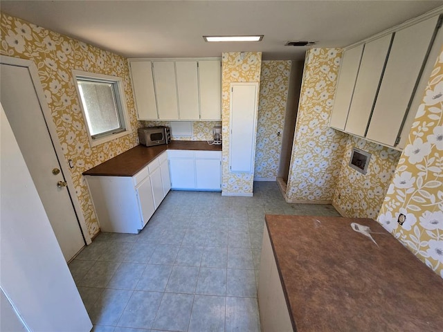 kitchen with light tile patterned floors, dark countertops, wallpapered walls, white cabinetry, and stainless steel microwave