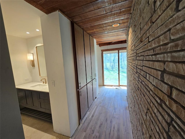 hallway featuring a sink, light wood-style floors, brick wall, and wooden ceiling