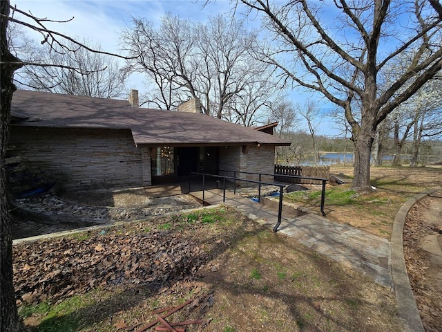 view of side of home featuring a patio, stone siding, a water view, and a chimney