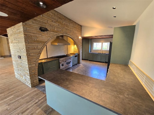 801 NE Ave C, Idabel, OK 74745 - kitchen with double oven range, wall chimney exhaust hood, arched walkways, dark countertops, and wood finished floors
