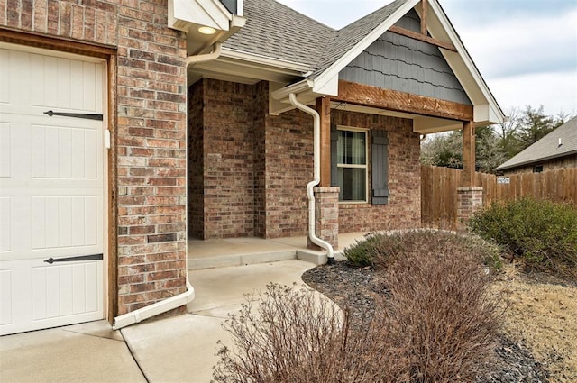 property entrance with brick siding, roof with shingles, and fence