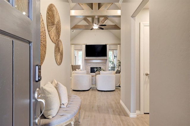 living area featuring beam ceiling, light wood-style flooring, a fireplace, baseboards, and ceiling fan