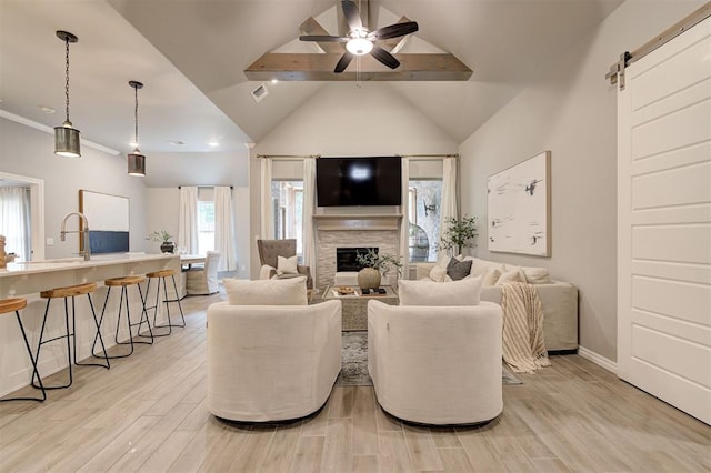 living room featuring beam ceiling, a ceiling fan, a barn door, a fireplace, and light wood finished floors