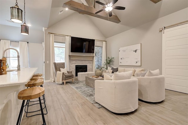 living room featuring visible vents, a barn door, light wood-style flooring, a fireplace, and a ceiling fan