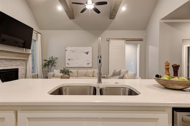 kitchen featuring a ceiling fan, a sink, open floor plan, a stone fireplace, and lofted ceiling