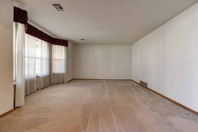 spare room with baseboards, light colored carpet, visible vents, and a textured ceiling