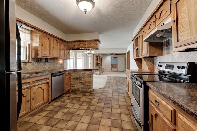 kitchen featuring dark countertops, brown cabinets, under cabinet range hood, and stainless steel appliances