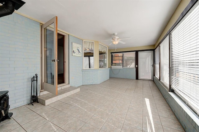 unfurnished sunroom featuring cooling unit, ceiling fan, and a wood stove