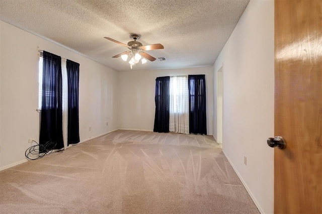 spare room with visible vents, baseboards, ceiling fan, light colored carpet, and a textured ceiling