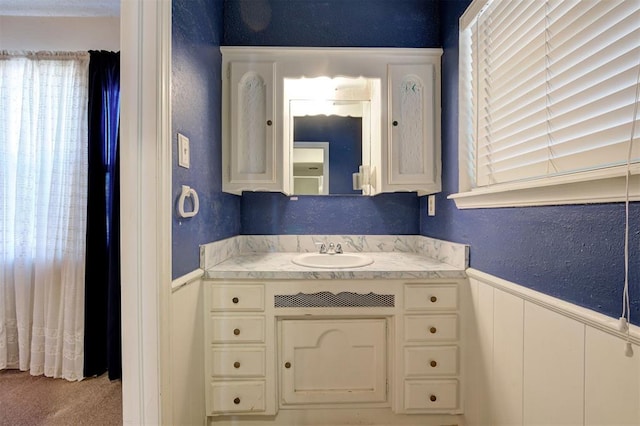 bathroom featuring wainscoting, vanity, and a textured wall