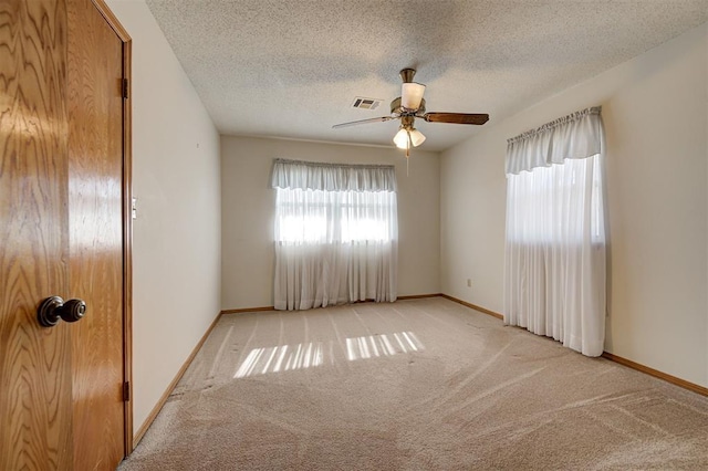 carpeted empty room featuring visible vents, a textured ceiling, baseboards, and a ceiling fan